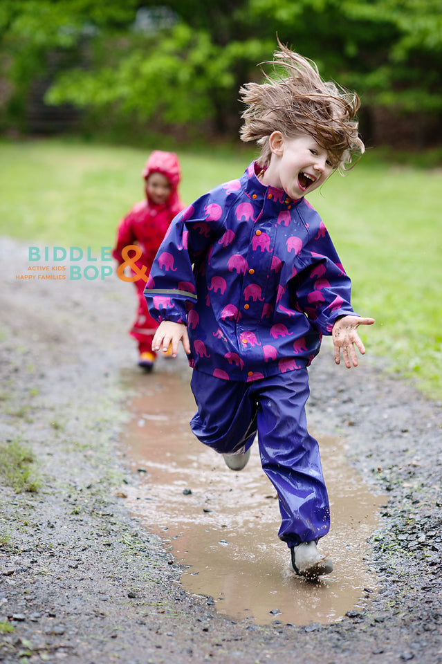 Child wearing waterproof rain gear set, playing outdoors in puddles. Shown in pattern, many colors available.