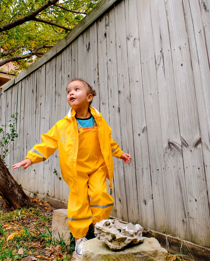 Young girl wearing waterproof rain gear set in yellow, playing outdoors